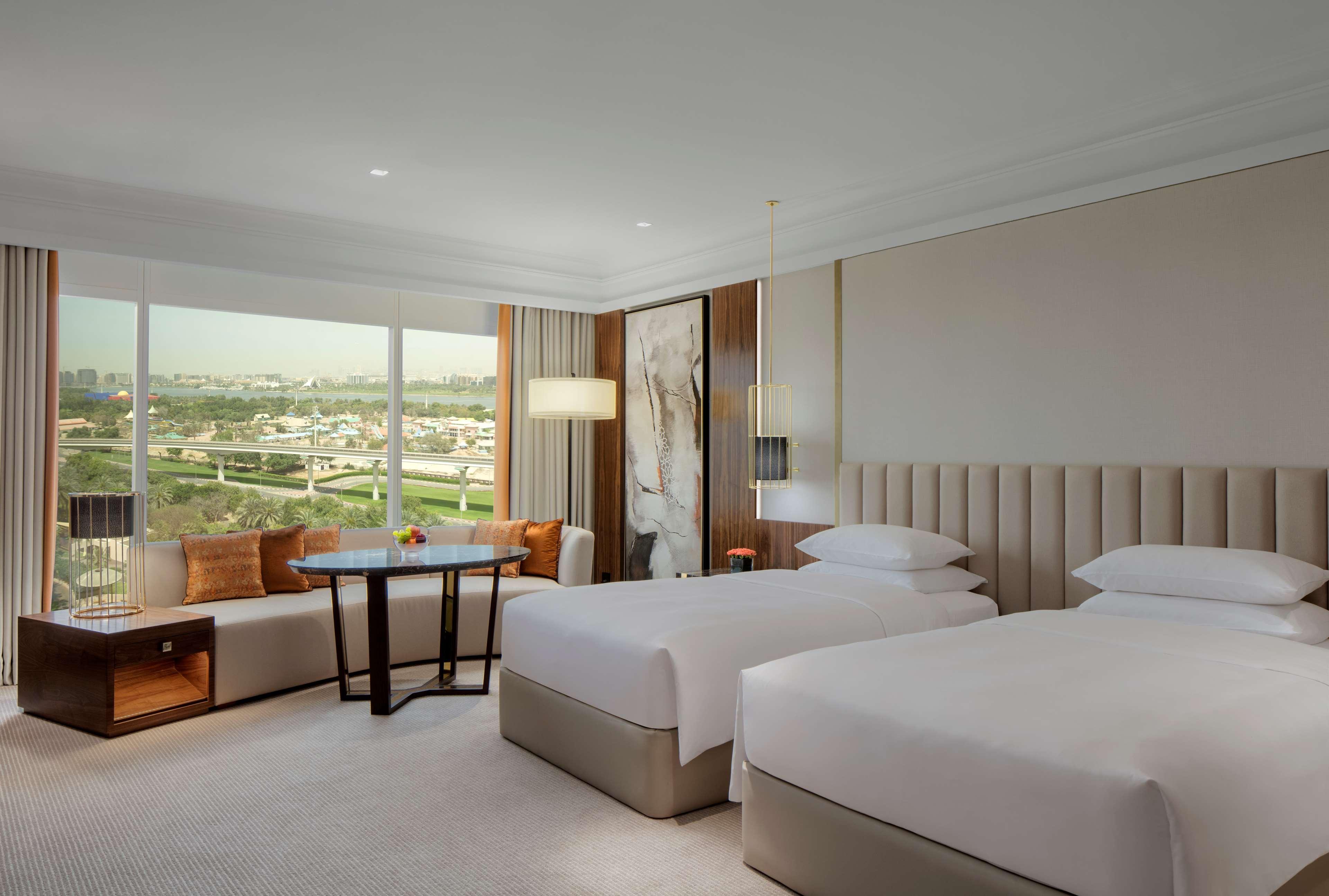 Hotel Grand Hyatt Dubai Esterno foto The photo shows a modern hotel room featuring two twin beds with white bedding. There is a large window providing a view of the outside landscape, allowing natural light to fill the space. The room is decorated in soft, neutral tones with modern furn