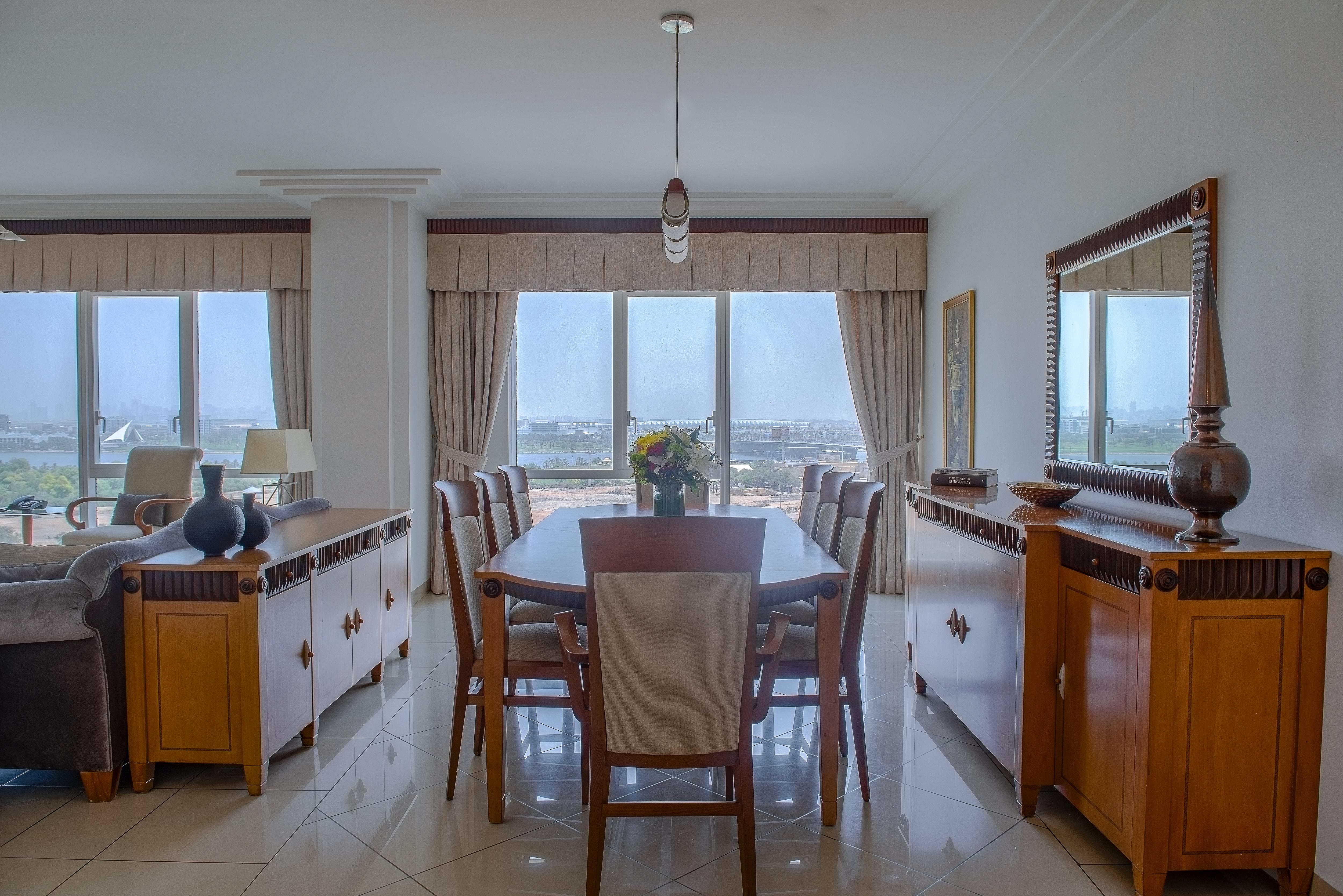 Hotel Grand Hyatt Dubai Esterno foto The photo displays a dining area featuring a stylish wooden dining table surrounded by chairs. The room is bright and airy, with large windows that offer a view of the outdoors. There are beige curtains framing the windows, and the flooring appears t