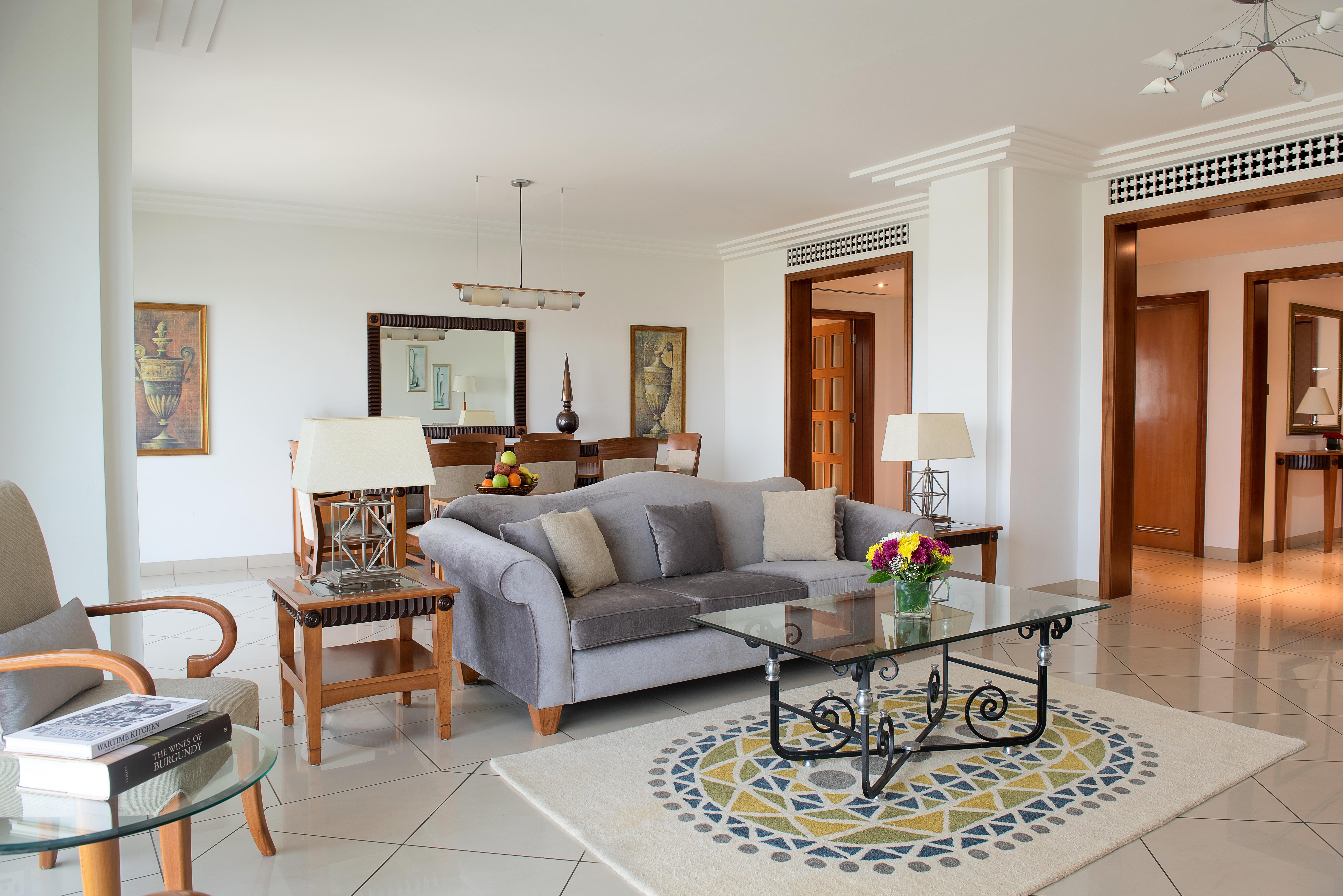 Hotel Grand Hyatt Dubai Esterno foto The photo shows a spacious and well-lit living room area. It features a light gray sofa with plush cushions, positioned around a glass coffee table with an ornate black metal base. A circular area rug with a decorative pattern is placed beneath the t