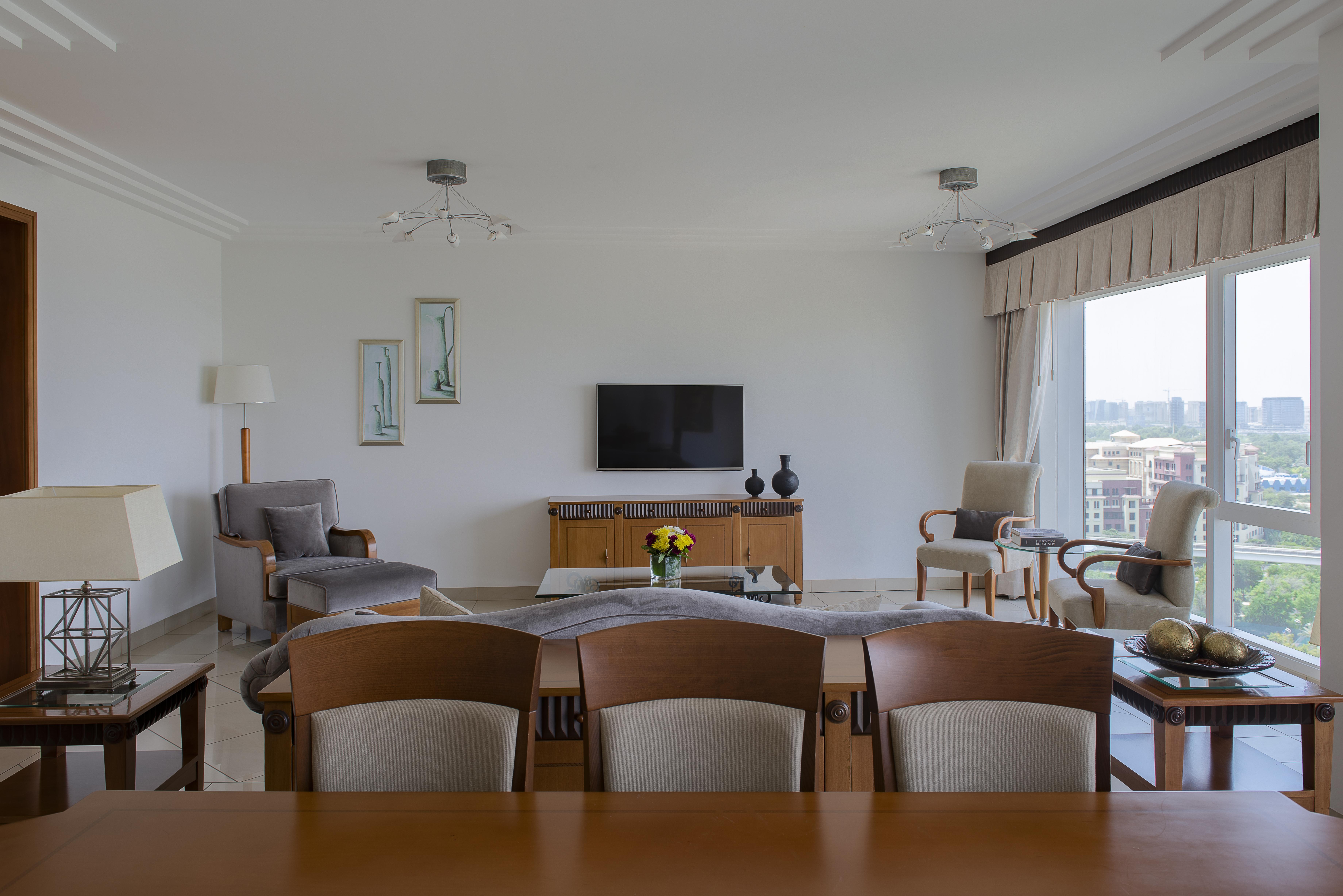 Hotel Grand Hyatt Dubai Esterno foto The photo shows a modern living room with a spacious and minimalistic design. There is a flat-screen television mounted on the wall, facing a seating arrangement that includes two armchairs and a sofa. A wooden table is positioned in the foreground, 