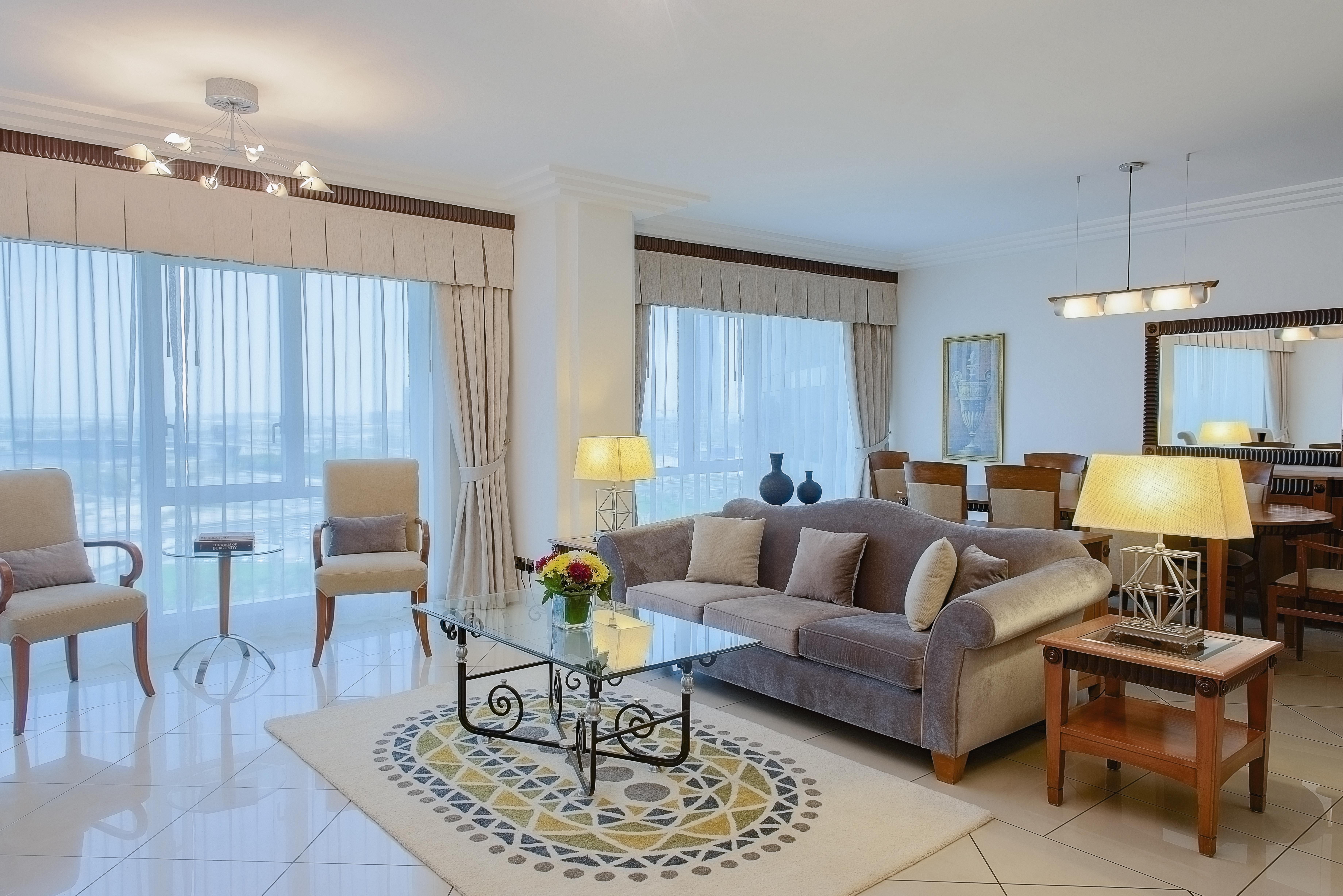 Hotel Grand Hyatt Dubai Esterno foto The photo shows a modern and stylish living room. It features a comfortable beige sofa with decorative pillows, a glass coffee table with an intricate base, and a small side table. There are two armchairs placed beside a floor lamp, creating a cozy s
