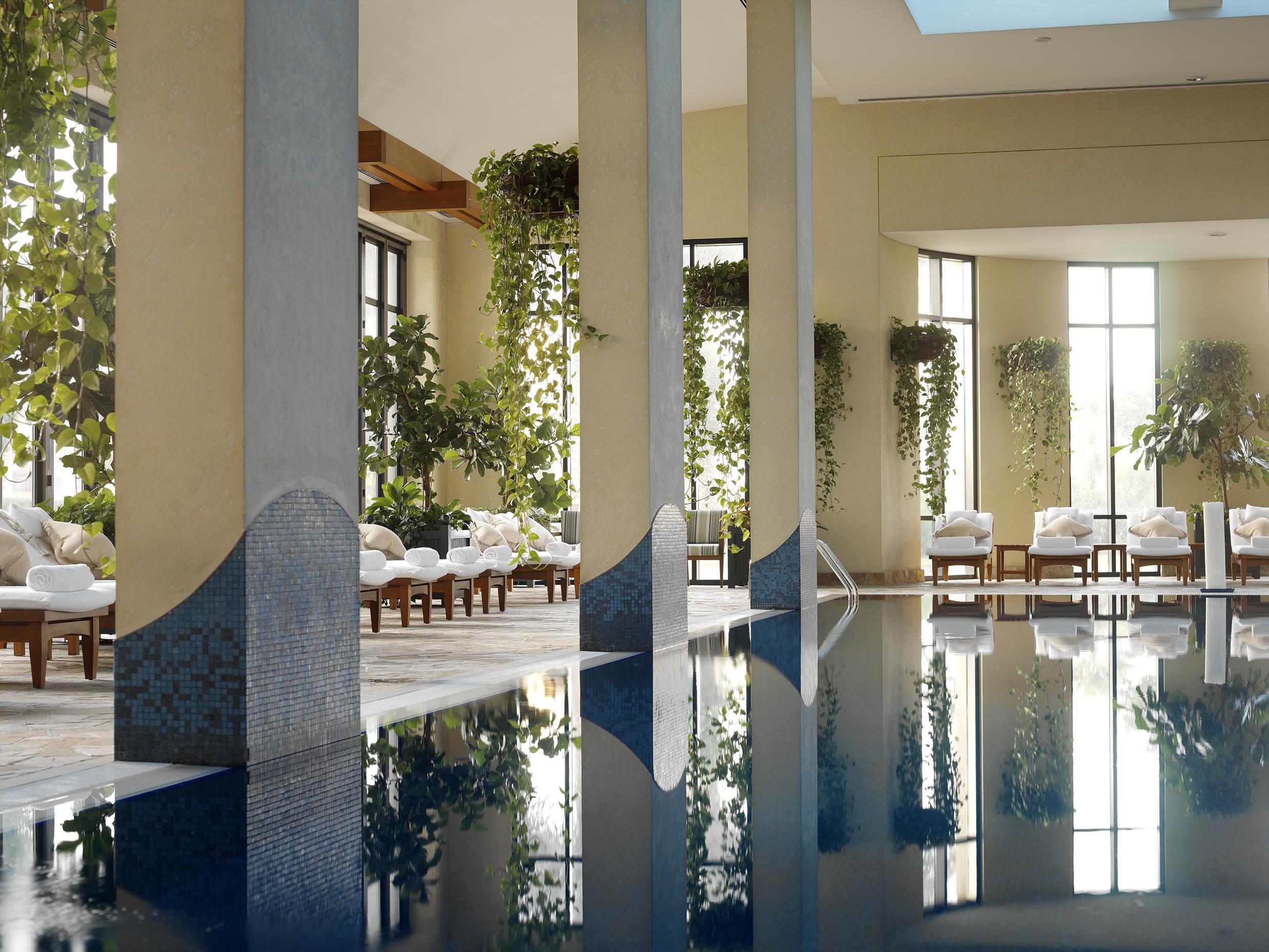 Hotel Grand Hyatt Dubai Servizi foto The image depicts a serene indoor swimming pool area. It features large windows allowing natural light to stream in, creating a bright and inviting atmosphere. The pool's calm waters reflect the surroundings, including decorative pillars and lush gre
