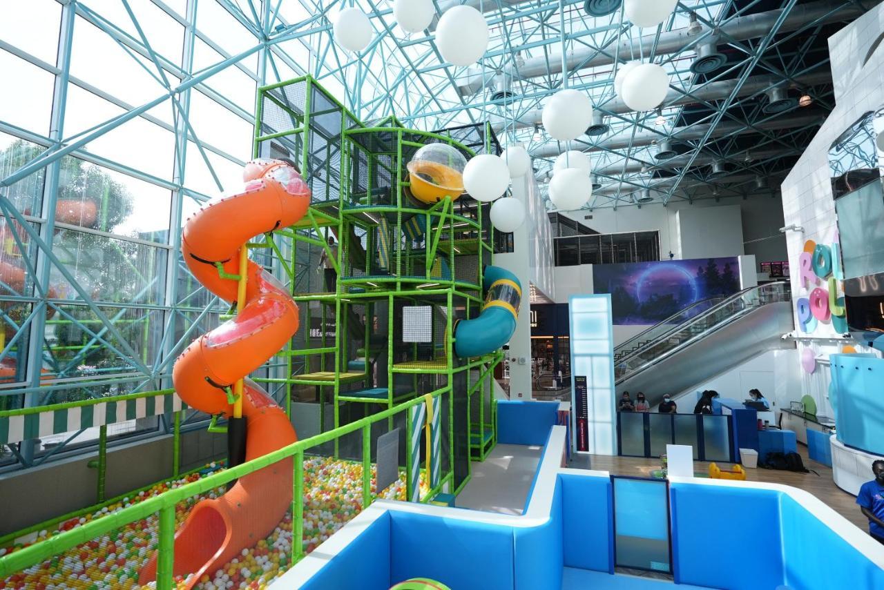 Hotel Grand Hyatt Dubai Esterno foto The photo shows an indoor play area with a modern, colorful design. It features two large water slides—one orange and one blue—leading from a multi-level climbing structure. The climbing structure is surrounded by green framework and includes various
