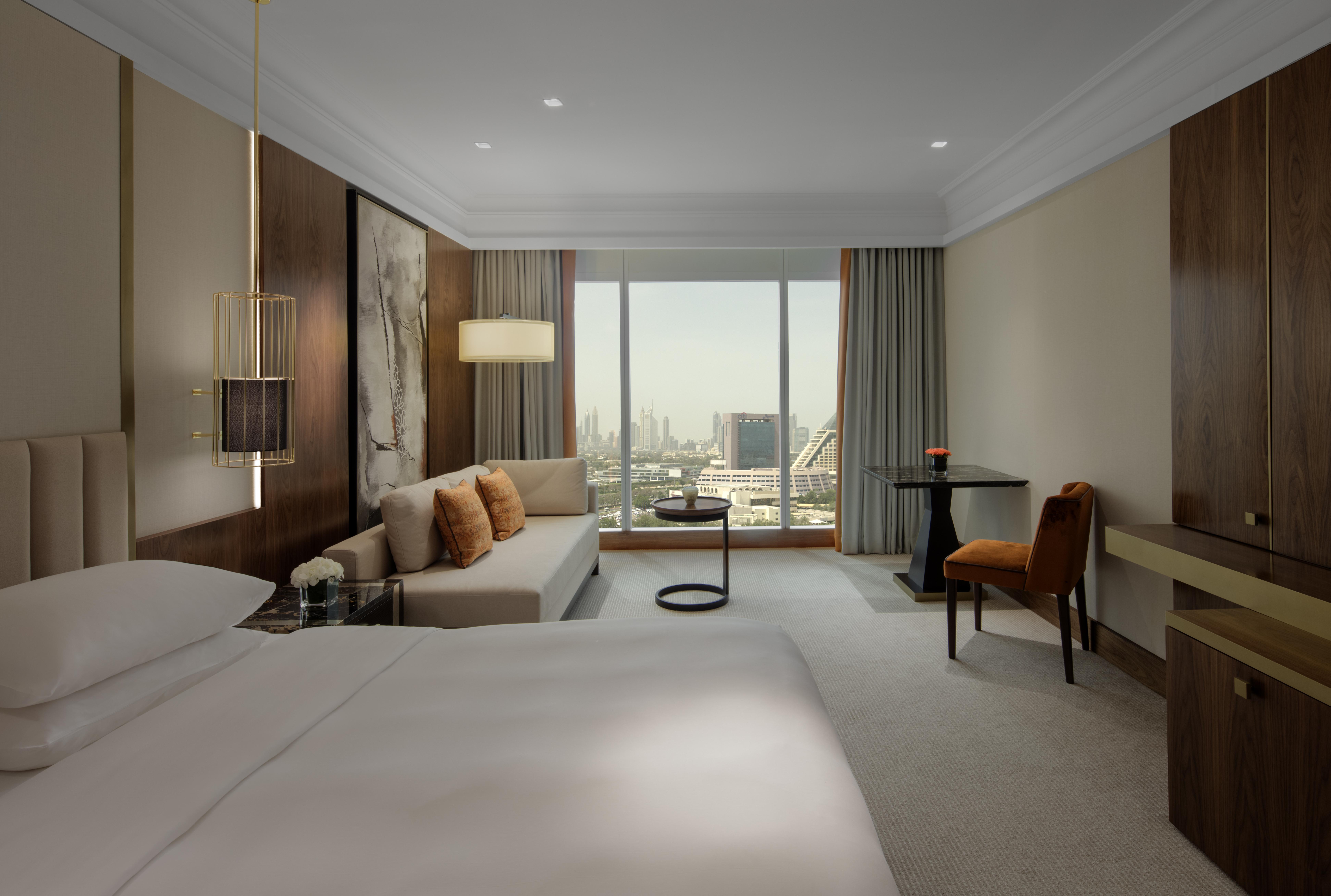 Hotel Grand Hyatt Dubai Esterno foto The photo depicts an elegant hotel room featuring a large bed with white linens. To one side, there is a comfortable sofa adorned with orange cushions, alongside a small round table. A modern chair is situated nearby, creating a cozy seating area. Th