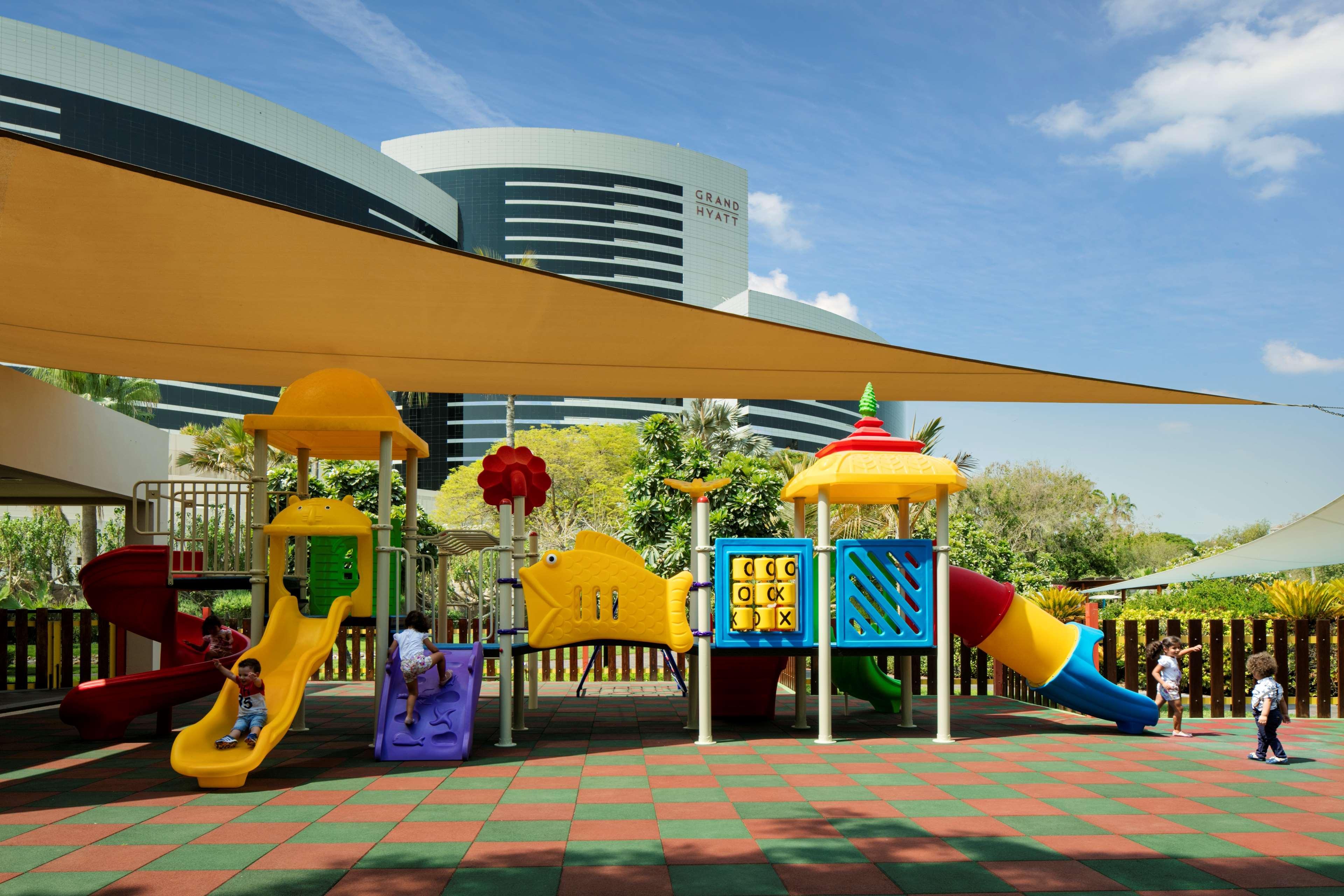 Hotel Grand Hyatt Dubai Esterno foto The image depicts a colorful playground designed for children. It features various play structures, including slides and climbing frames, in vibrant colors such as yellow, purple, and red. There's also a shaded area with a large canopy to protect fro