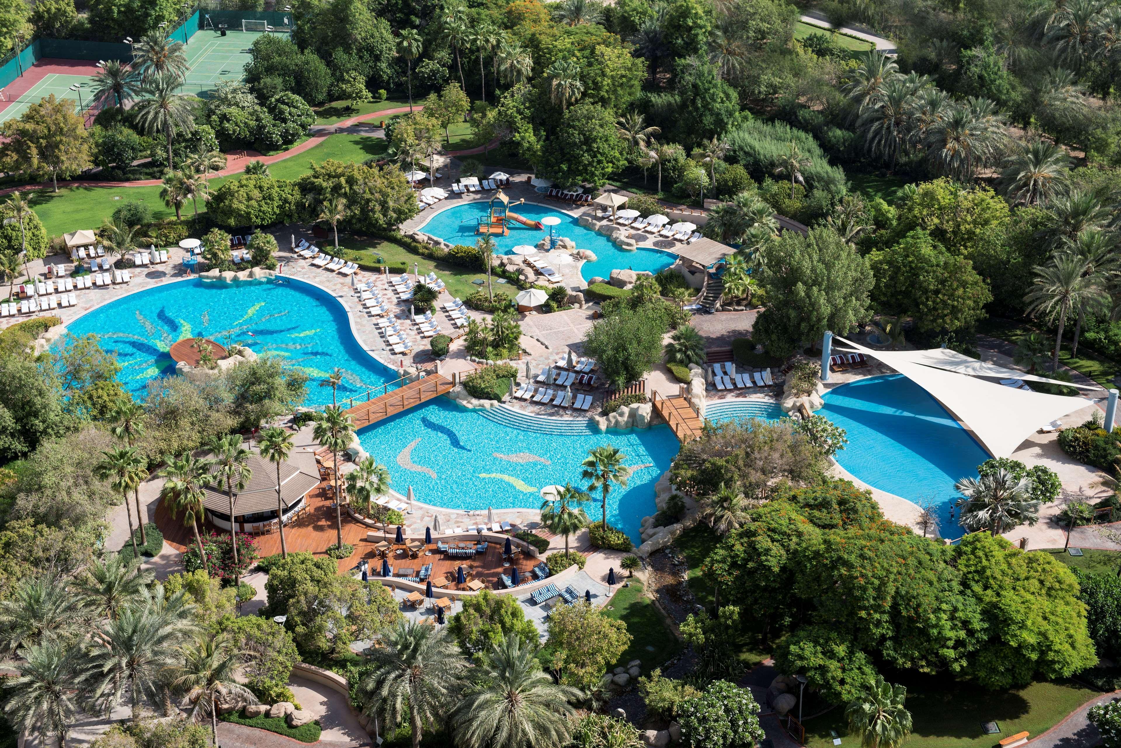 Hotel Grand Hyatt Dubai Esterno foto The photo shows a beautiful aerial view of a luxurious pool area surrounded by lush greenery. There are several interconnected swimming pools of different shapes and sizes, with sun loungers arranged around them. The pools feature various elements su