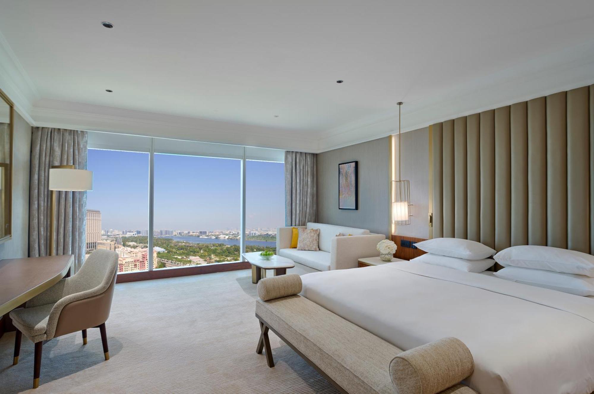 Hotel Grand Hyatt Dubai Esterno foto The photo shows a modern hotel room featuring large windows with a view. The room is designed with a neutral color palette and elegant furnishings. There are two beds neatly made, a sofa area, and a small table. Soft lighting fixtures are present, an