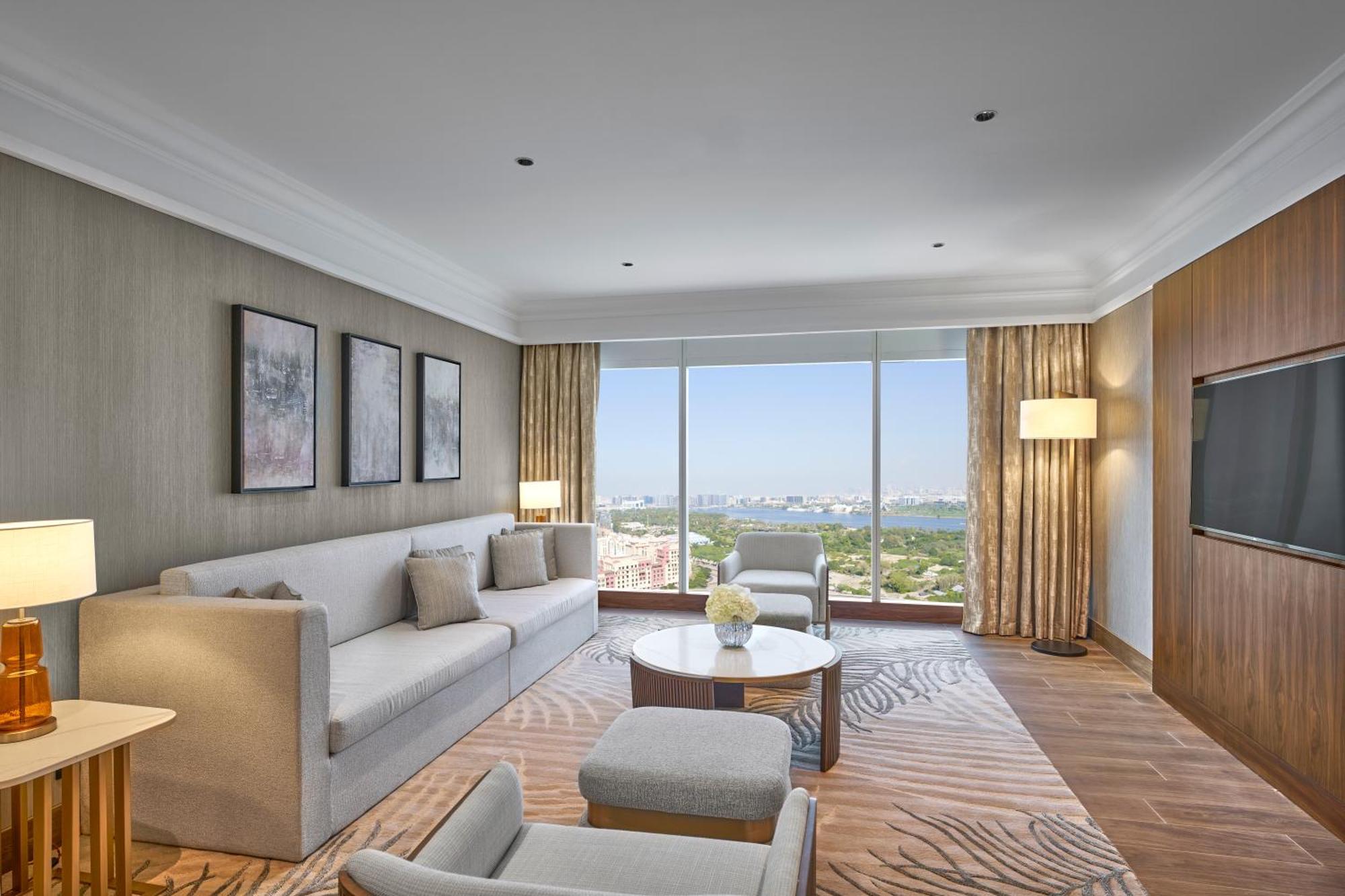 Hotel Grand Hyatt Dubai Esterno foto The photo shows a modern hotel room featuring a comfortable living area. There is a light-colored sofa with several cushions, a coffee table in the center, and a couple of armchairs. The walls are adorned with framed artworks, and large windows provi
