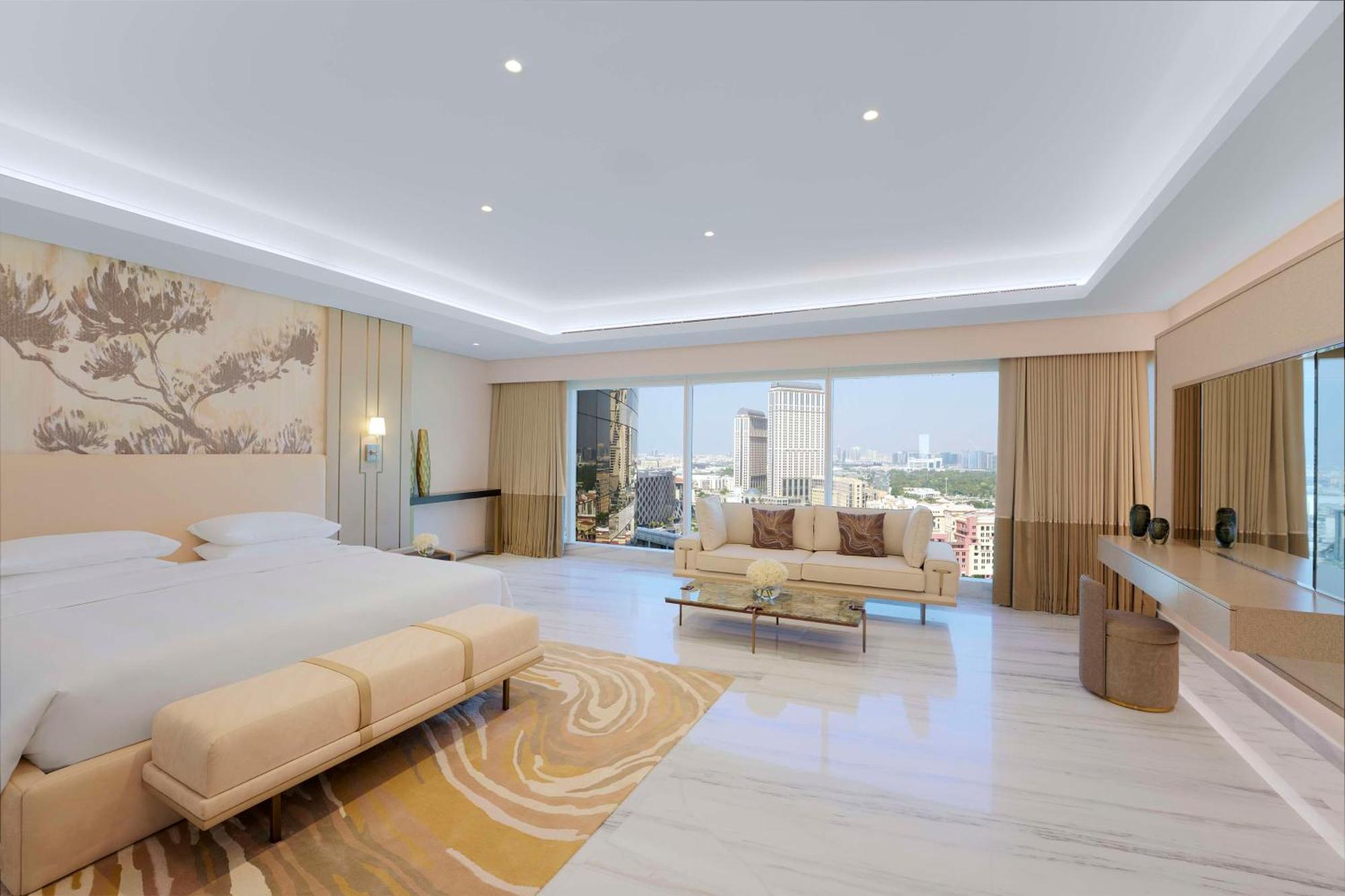Hotel Grand Hyatt Dubai Esterno foto The image shows a spacious hotel room that features a contemporary design. It has a large window that offers a view of the city skyline, allowing natural light to fill the space. The room includes a cozy seating area with a light-colored sofa and a s