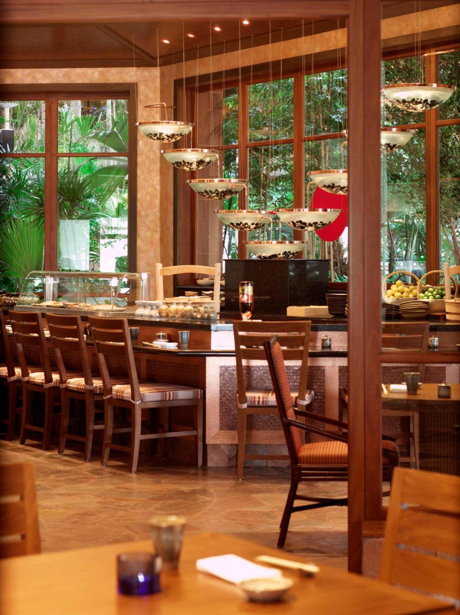Hotel Grand Hyatt Dubai Esterno foto The photo shows the interior of a restaurant or dining area with a warm and inviting ambiance. There is a long wooden bar with several empty chairs arranged in front of it. The bar features sleek, modern light fixtures hanging above, and there are va