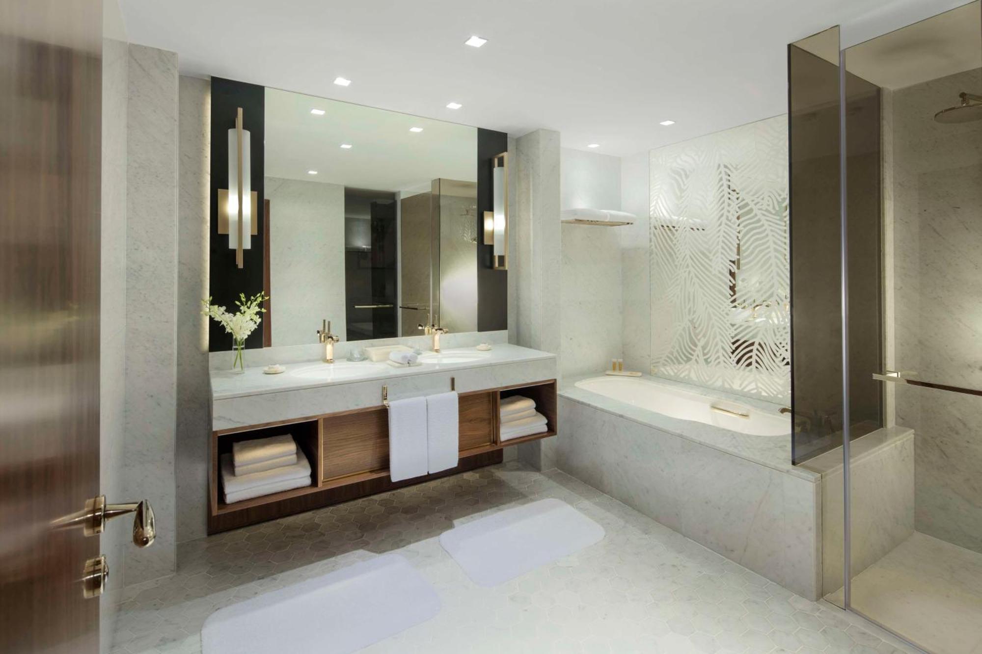 Hotel Grand Hyatt Dubai Esterno foto The photo shows a modern bathroom design featuring a sleek and minimalist aesthetic. It includes:

- A large, double vanity with a white countertop and two sinks, enhanced by stylish gold faucets.
- Above the vanity, there is a spacious mirror that r