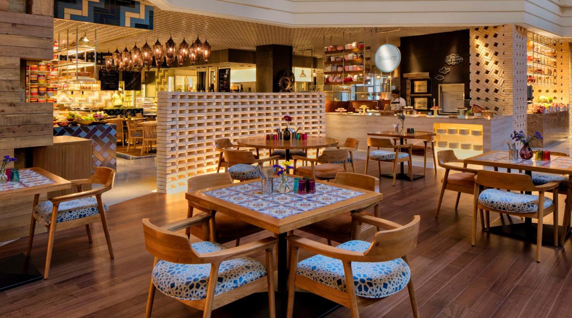 Hotel Grand Hyatt Dubai Esterno foto The photo shows an elegant restaurant interior. It features wooden flooring and modern decor. The seating is centered around wooden tables with patterned surfaces and comfortable chairs. There are decorative elements, such as vases with colorful flow