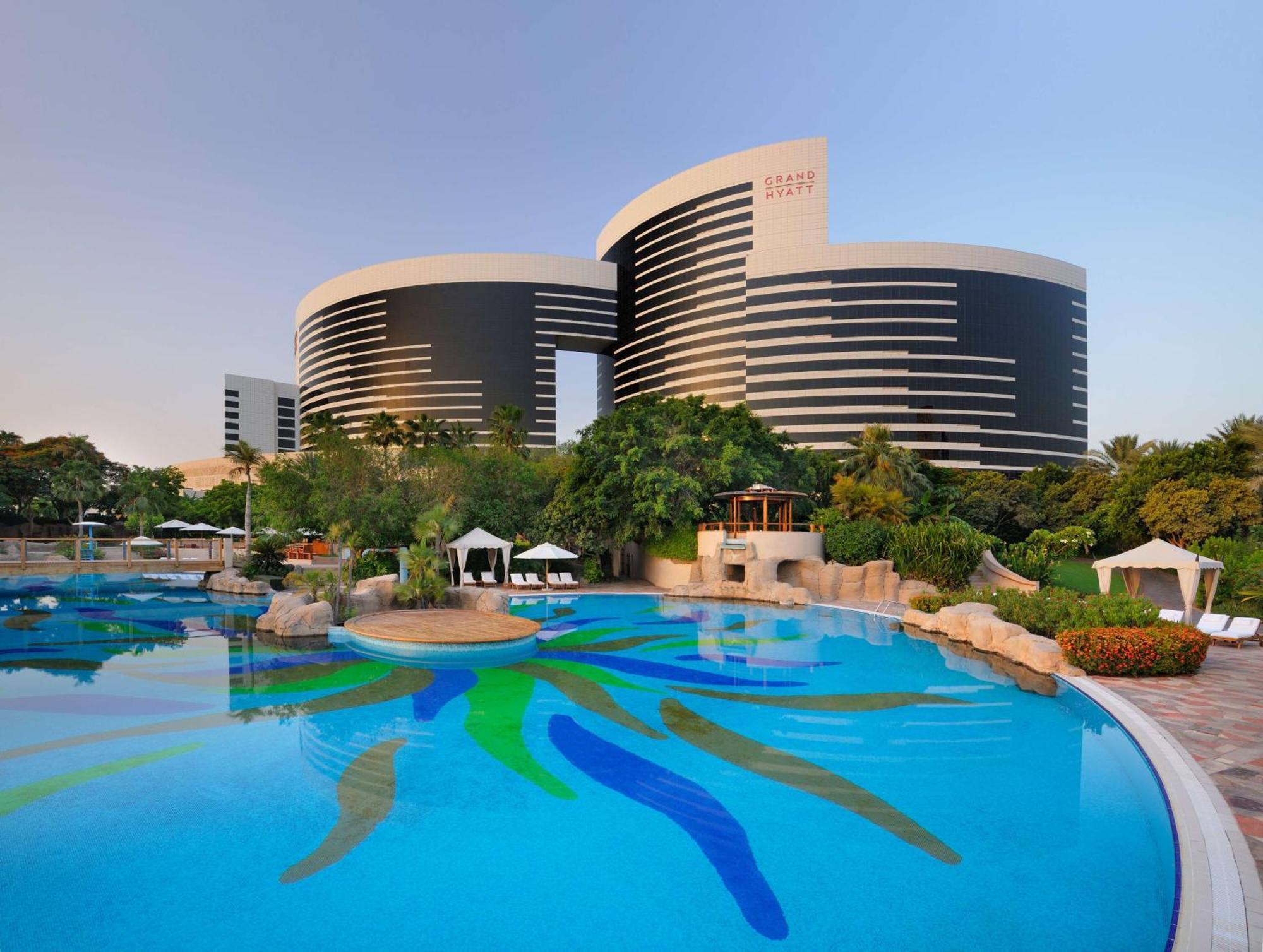 Hotel Grand Hyatt Dubai Esterno foto The photo shows a modern architectural structure, likely a hotel or resort, characterized by two circular buildings with a sleek, contemporary design. The buildings are black and white with horizontal stripes and appear to have large windows. In the 