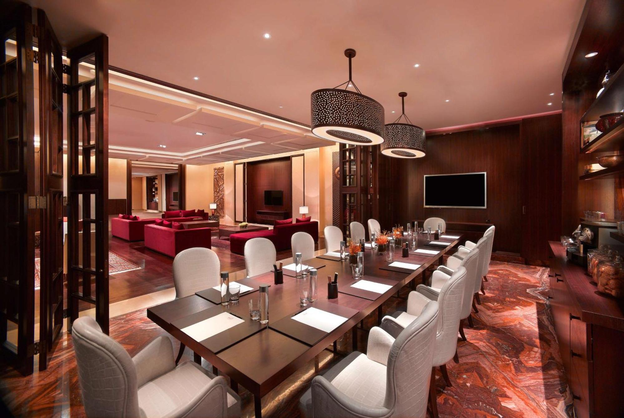 Hotel Grand Hyatt Dubai Esterno foto The photo shows an elegant dining or conference room. It features a long wooden table surrounded by white, upholstered chairs. The table is set with notepads and pens, indicating it may be used for meetings. There are two stylish light fixtures hangi