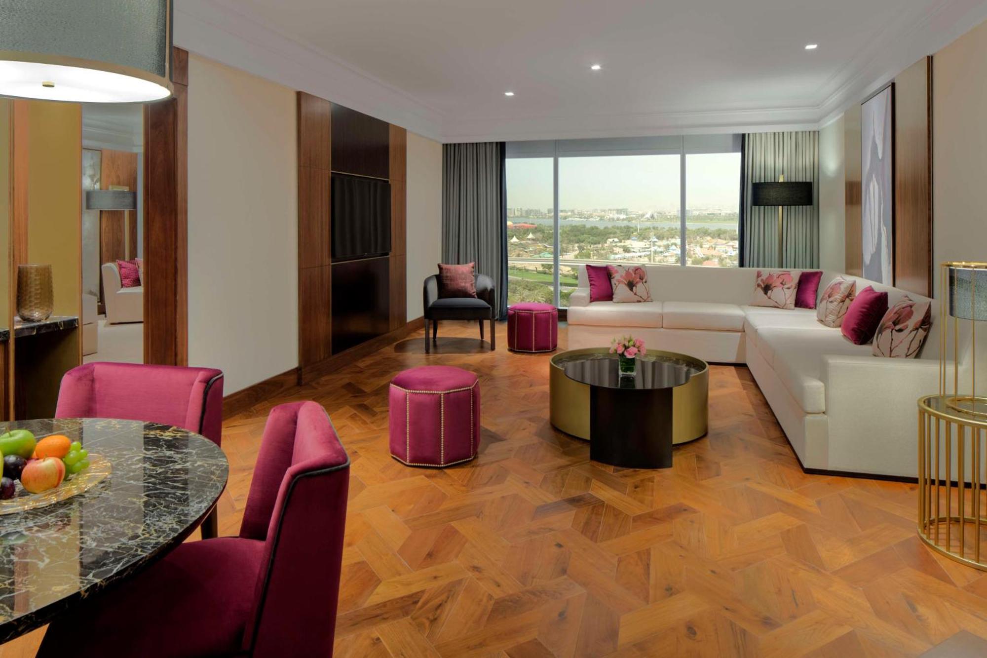 Hotel Grand Hyatt Dubai Esterno foto The photo shows a modern and stylish living space. There is a large, L-shaped white sofa adorned with pink and purple cushions, complemented by a round black coffee table in the center. In front of the sofa, there are two round ottomans in a matching